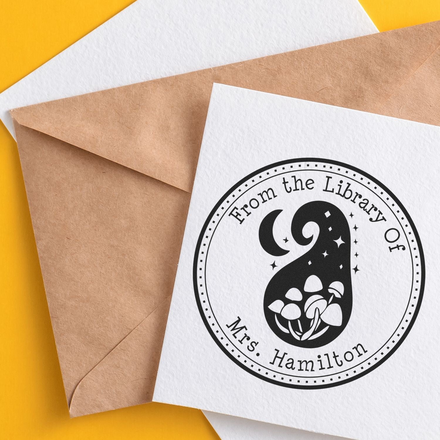 Black custom library stamp seal on white card over kraft envelopes, with yellow background and floral number 9 design.