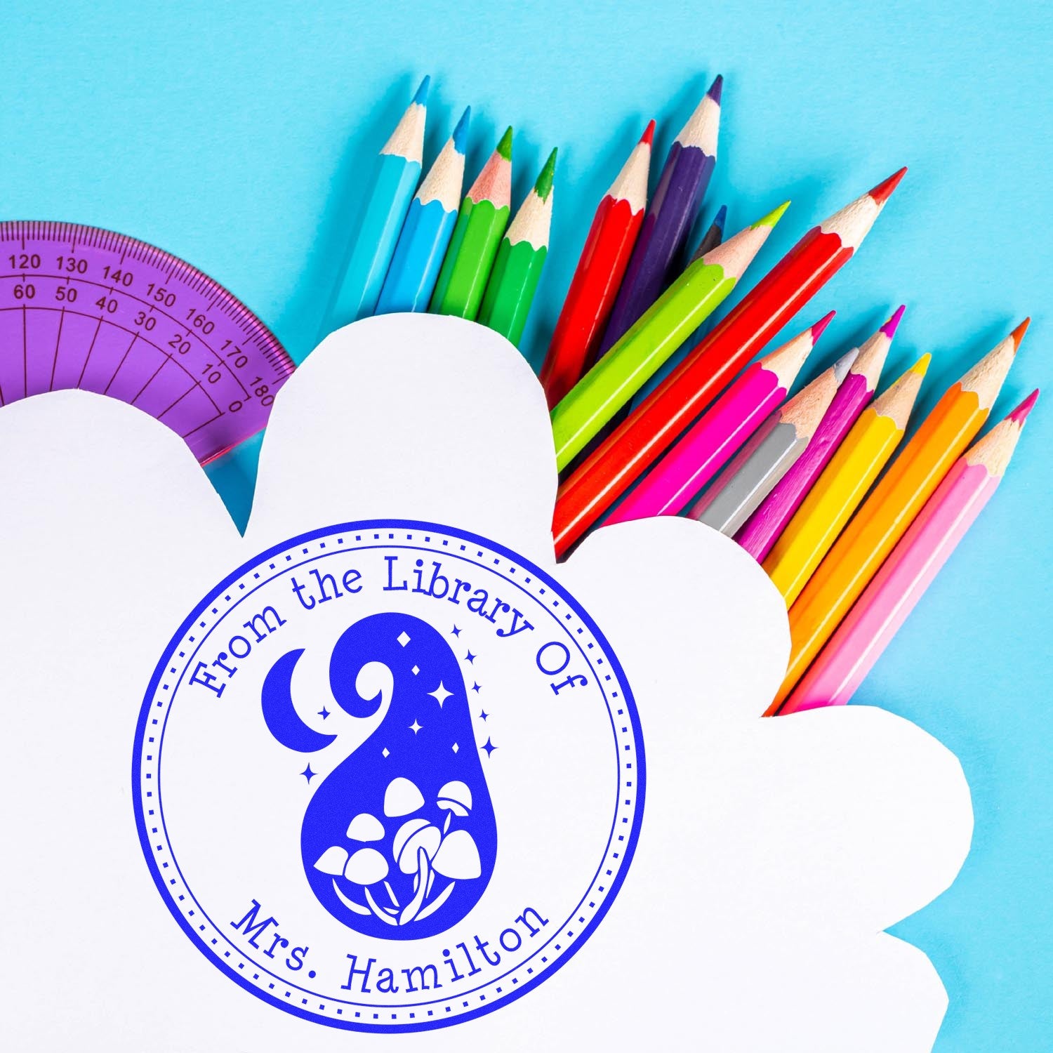 Custom blue library seal stamp on white flower-shaped paper, with colorful pencils and a purple protractor on a blue background.