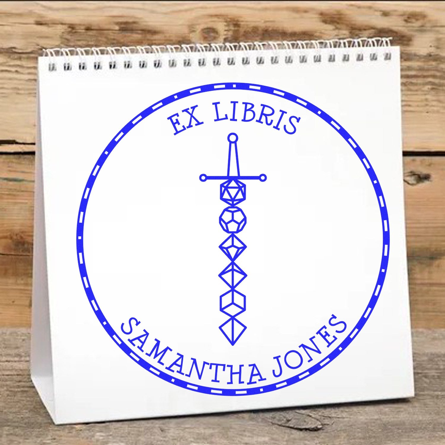 Blue ex libris stamp seal with geometric sword design and Samantha Jones on a white paper bag.