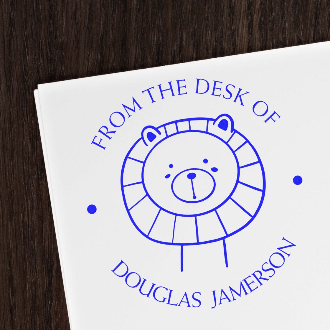 FlutterPaws cartoon animal self-inking custom-made stamp featuring a cute lion design with the text 'From the Desk of Douglas Jamerson.' This personalized address stamp is shown on white paper against a dark wood background.