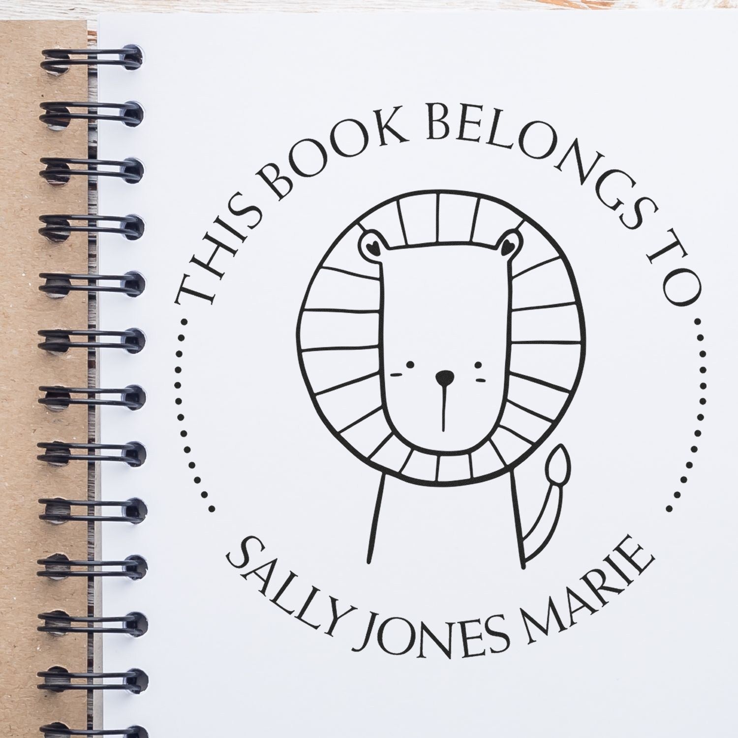 Slim Pre-Inked ZippyZap Cartoon Animal Custom Book Personalization Stamp featuring a cute lion design on a notebook page. Text reads "This Book Belongs To Sally Jones Marie." Ideal for a customizable new address stamper.