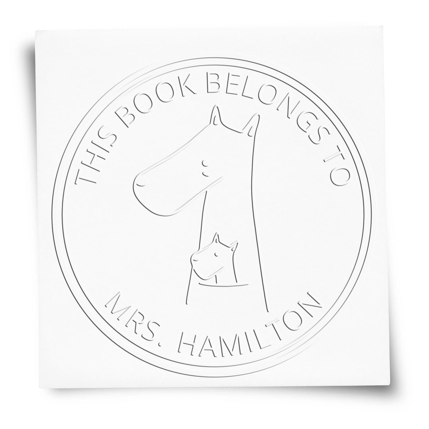Custom Home Stamp featuring a MuddleMoo cartoon animal design embossed on paper. The custom-made embossing seal displays a large animal with a smaller one inside, surrounded by the text 'This Book Belongs To Mrs. Hamilton.'