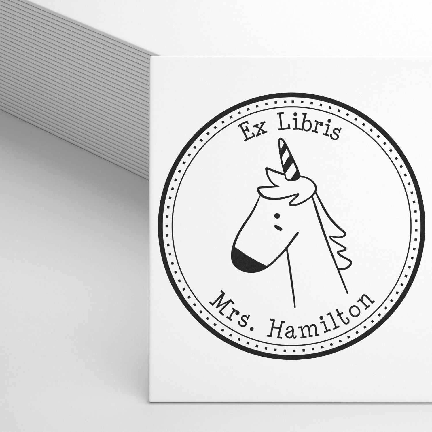 Slim Pre-Inked GlimmerGlide Cartoon Animal Custom Bookplate Template Stamp featuring a unicorn design with "Ex Libris" and "Mrs. Hamilton" text. Ideal for a Personalized Return Mail Stamper, shown on a white card next to a stack of paper.