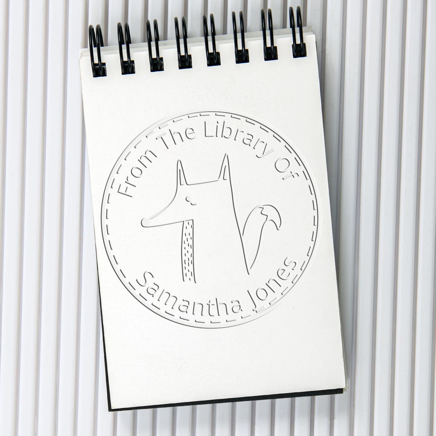 CuddleCub Cartoon Animal Handheld Personalized Book Lover Gift Embosser displayed on a notepad. The design features a custom-made address stamp with a cute animal illustration and the text "From The Library Of Samantha Jones."