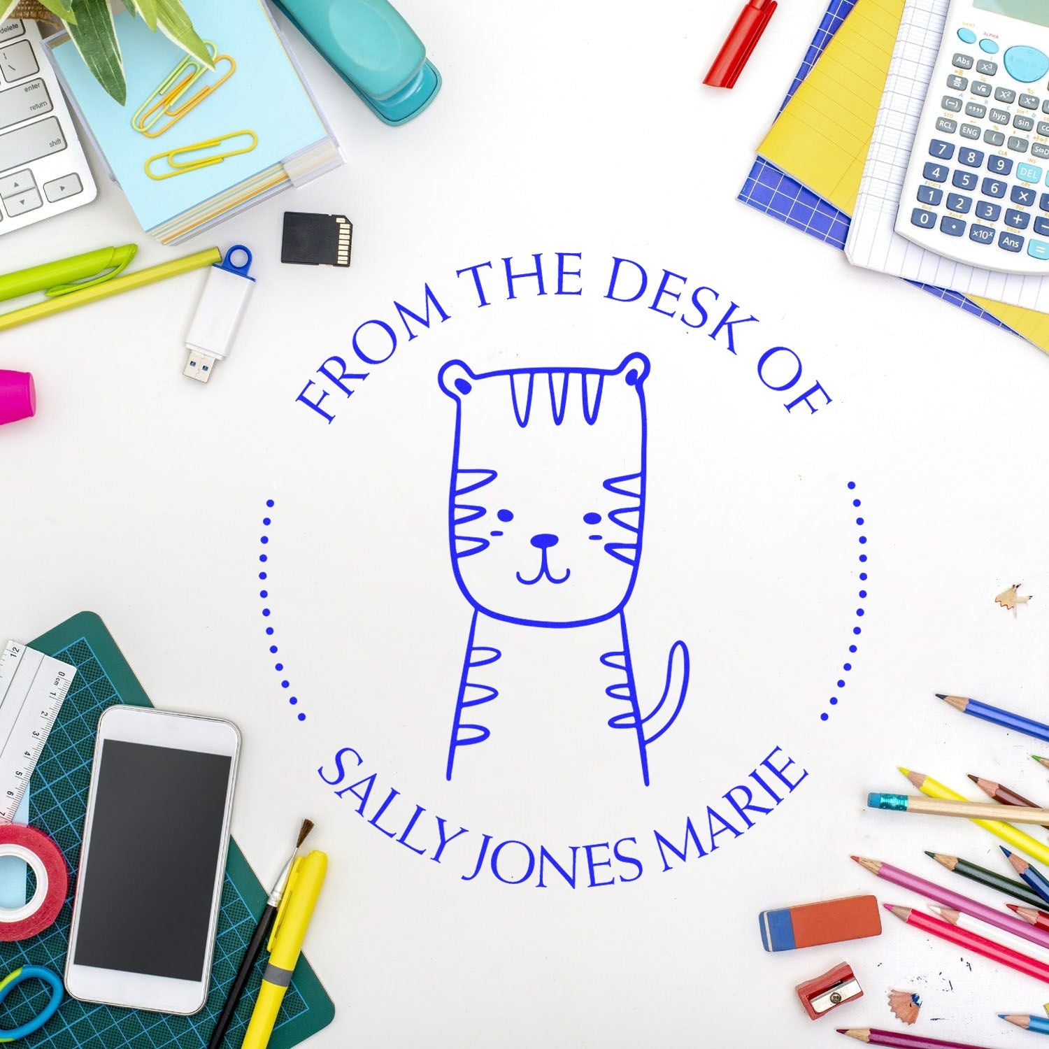 A Slim Pre-Inked TizzyTumble Cartoon Animal Custom Ex Libris Design Stamp featuring a cute cat is displayed on a desk surrounded by stationery. The Custom-Made Mailing Stamp reads "From the Desk of Sally Jones Marie" in blue ink.