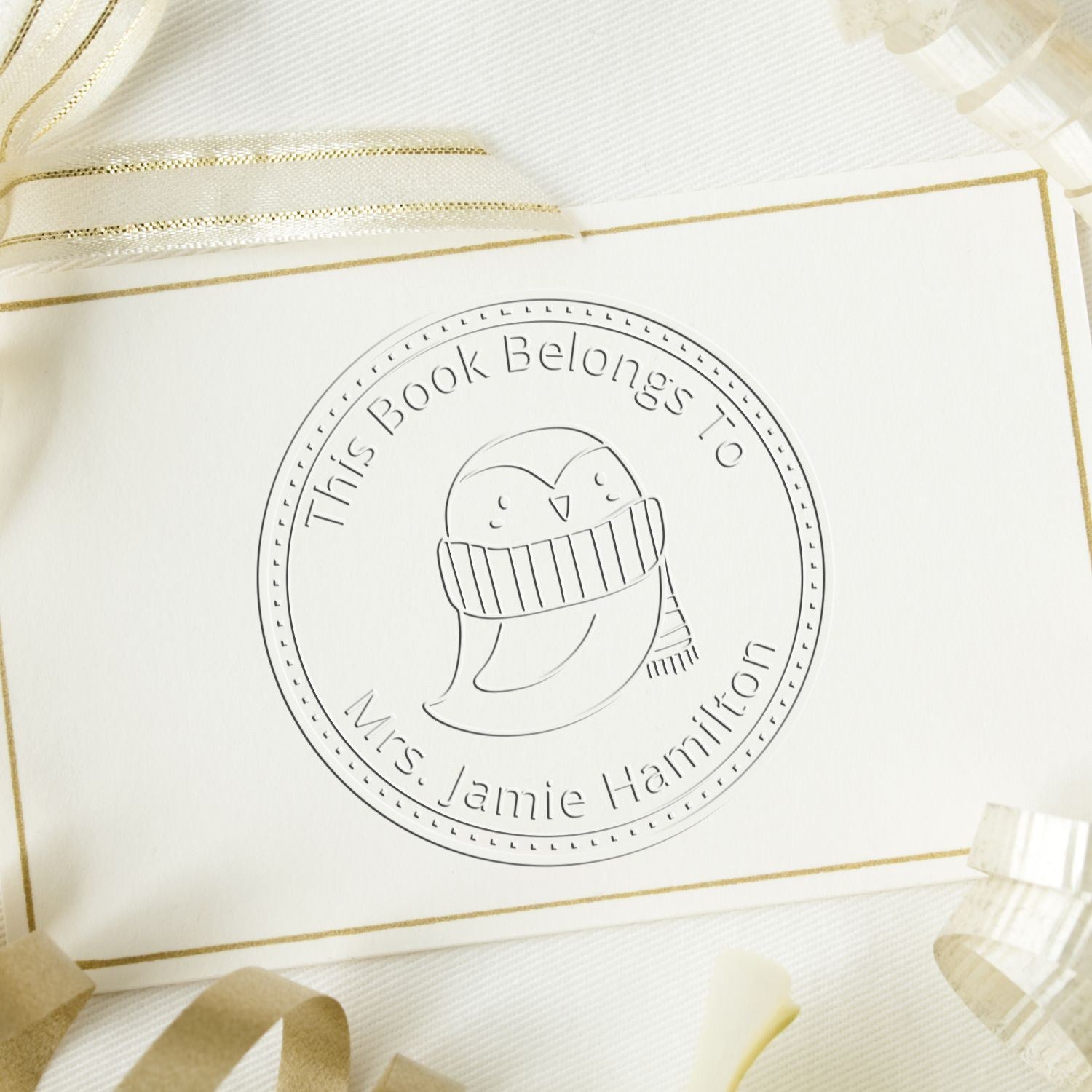 QuirkyQuack cartoon animal embosser on a library book page, featuring a personalized "This Book Belongs To" design. Includes a personalizable address stamp, surrounded by decorative ribbons on a textured background.