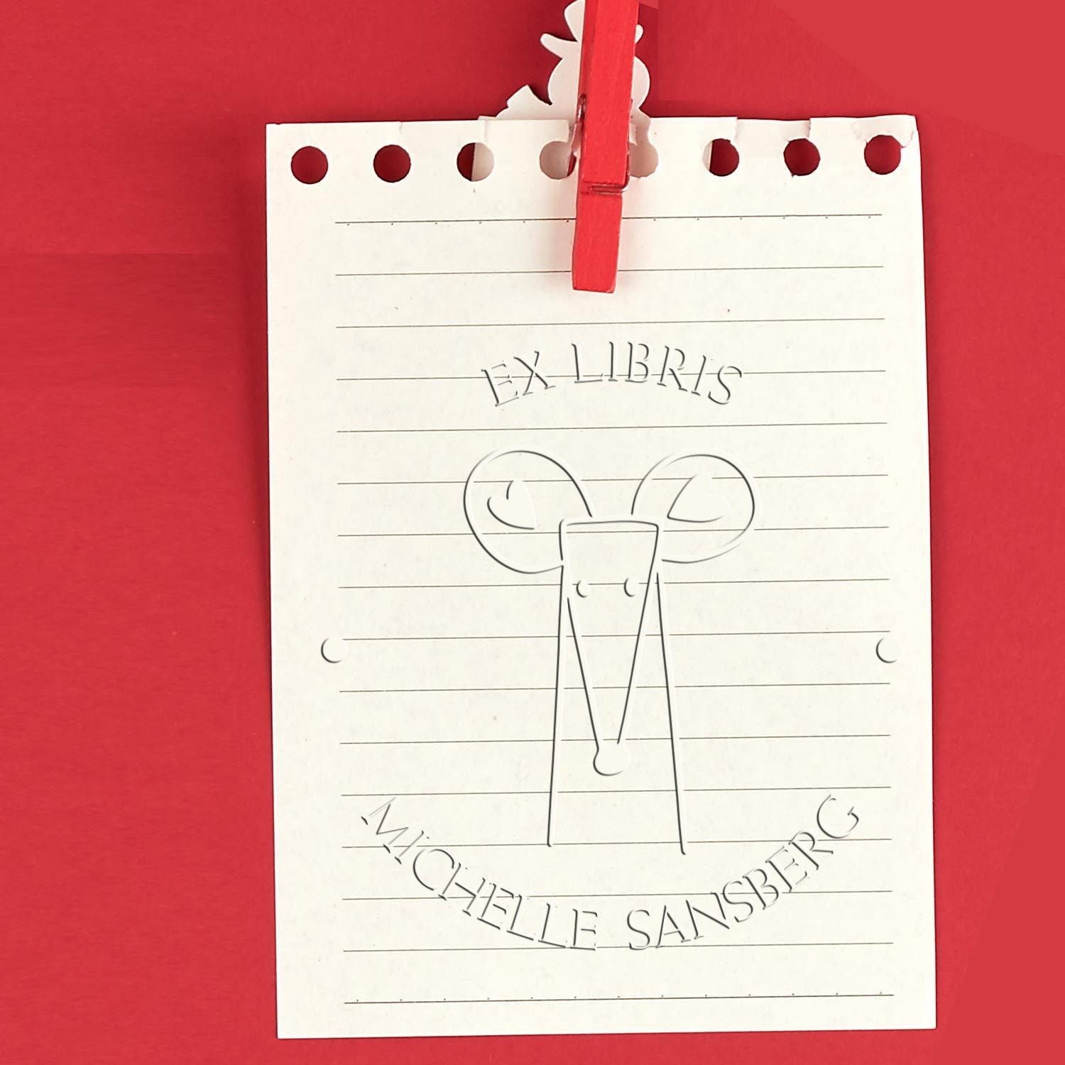 DazzleDash cartoon animal design on a personalized library book "Belongs To" seal, featuring a custom-made new address stamper. The seal is on lined paper clipped with a red clothespin against a red background.