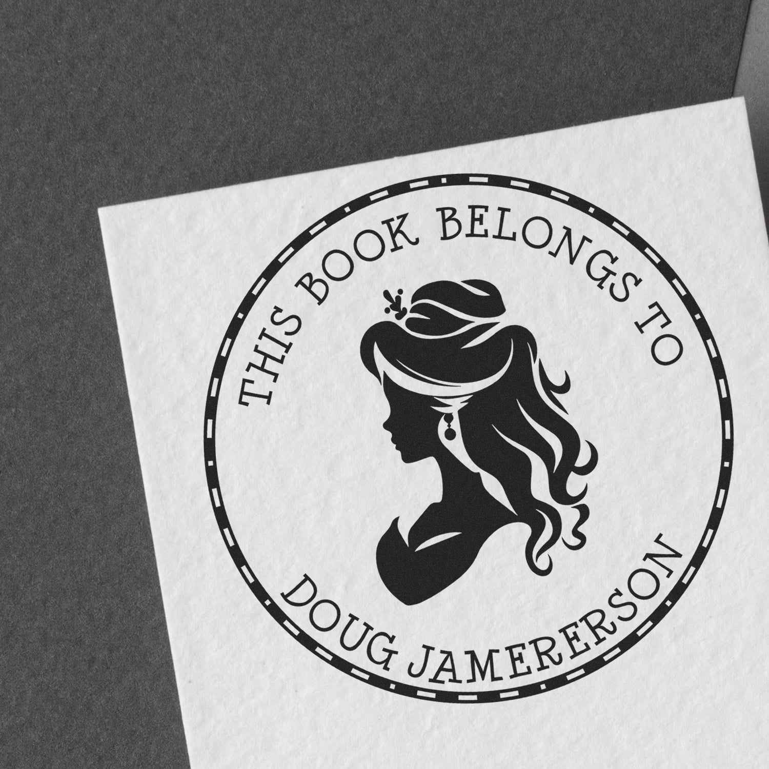 Black custom book stamp seal with woman silhouette and text This Book Belongs to Doug Jamerson on white paper.