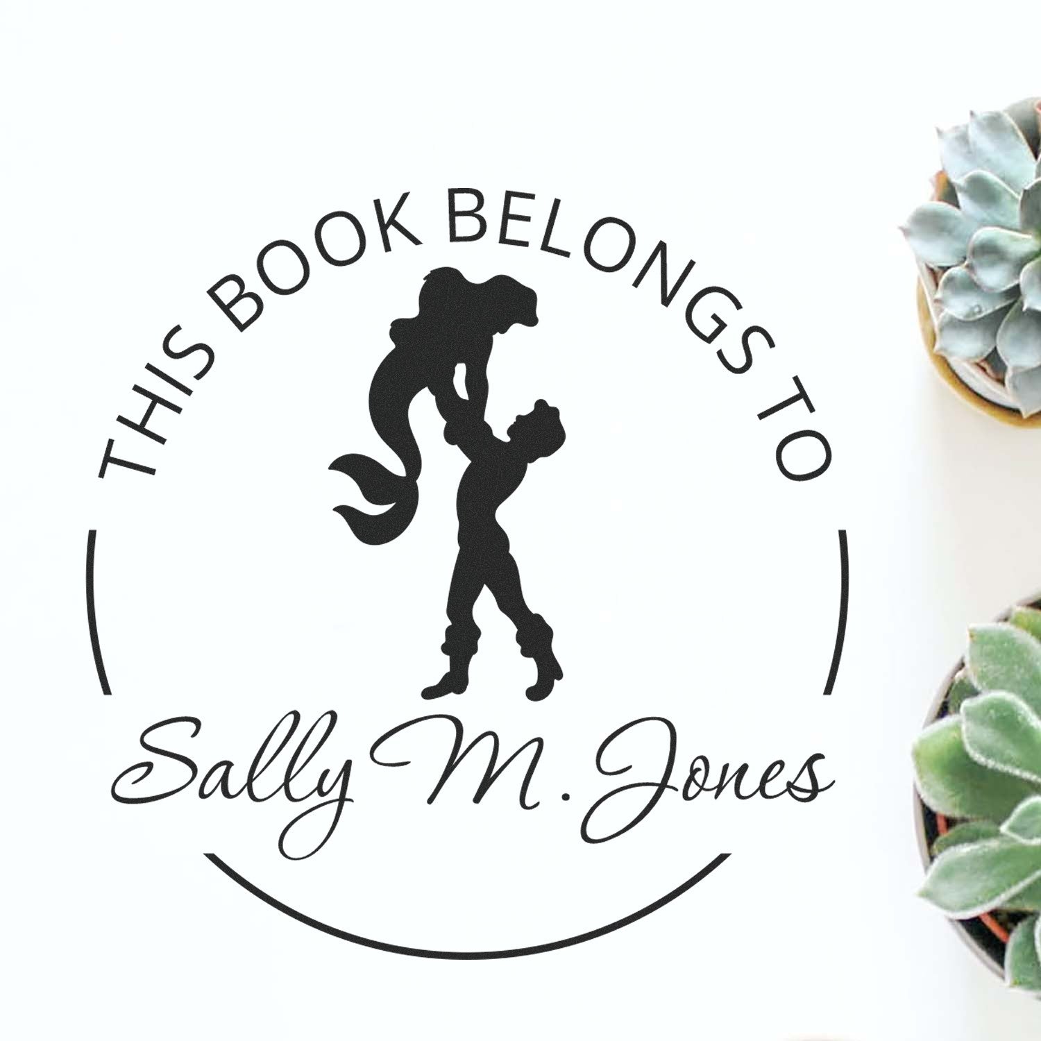 Black personalized book stamp seal with mermaid silhouette and This Book Belongs to Sally-M. Jones on white, with succulents.