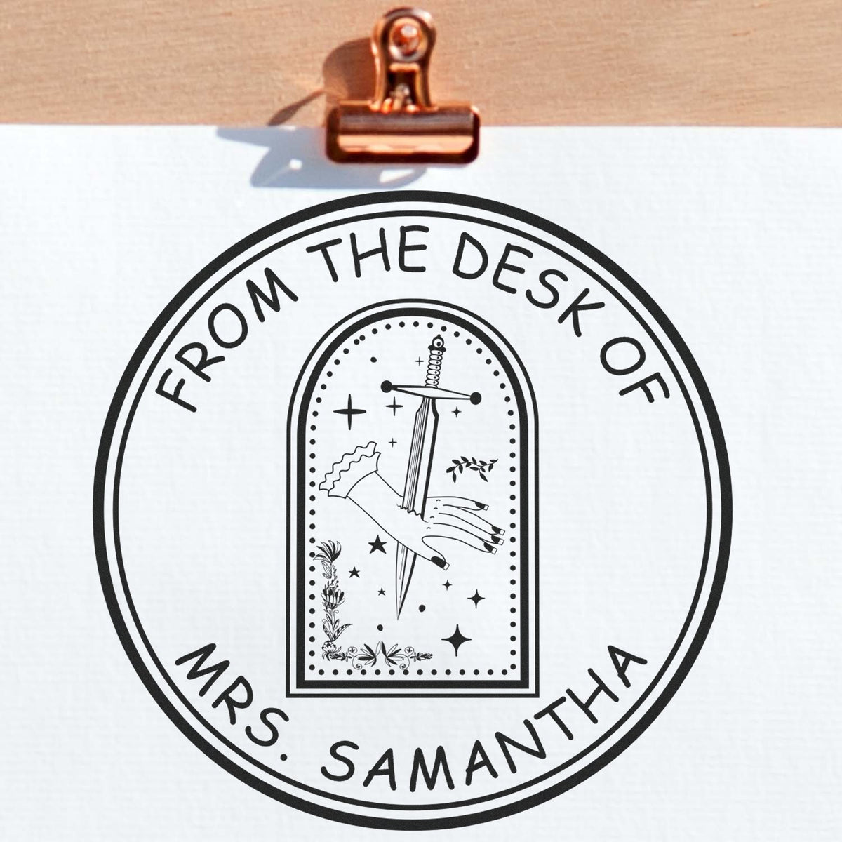 Black custom round stamp seal reading From the Desk of Mrs. Samantha, with sword and hand design, clipped on white paper.