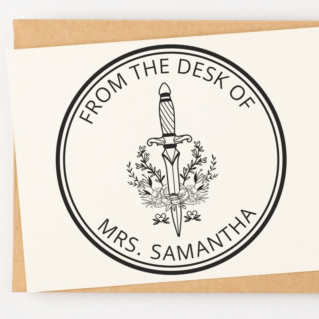 Custom black desk stamp seal with sword and floral wreath on cream card, reading From the Desk of Mrs. Samantha.