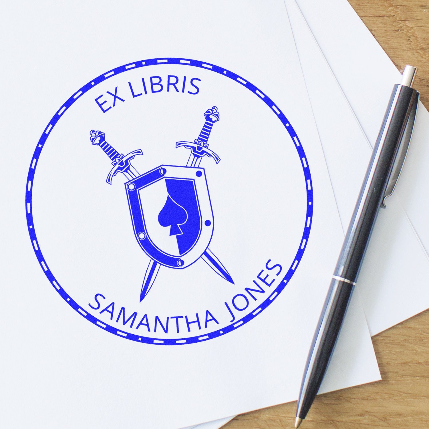 Blue ex libris stamp and seal with shield, crossed swords, and Samantha Jones on white paper beside a black pen.