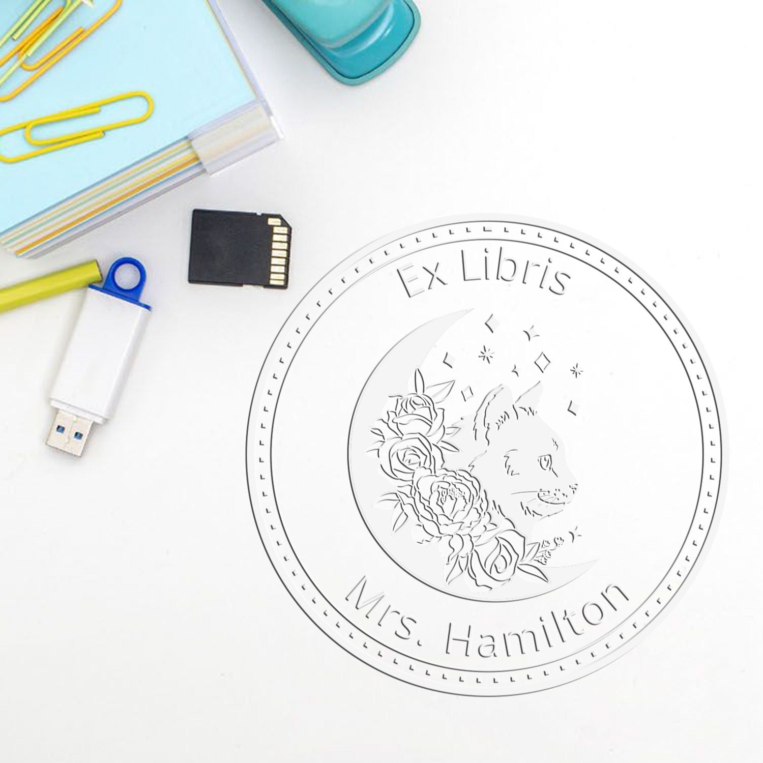 Custom white Ex Libris stamp seal with wolf and roses, beside a USB drive, memory card, and pastel stationery on white.