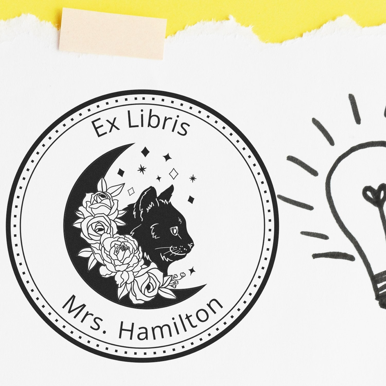 Black Ex Libris stamp seal with cat, roses and crescent moon on white paper, accented by yellow torn-edge strip.