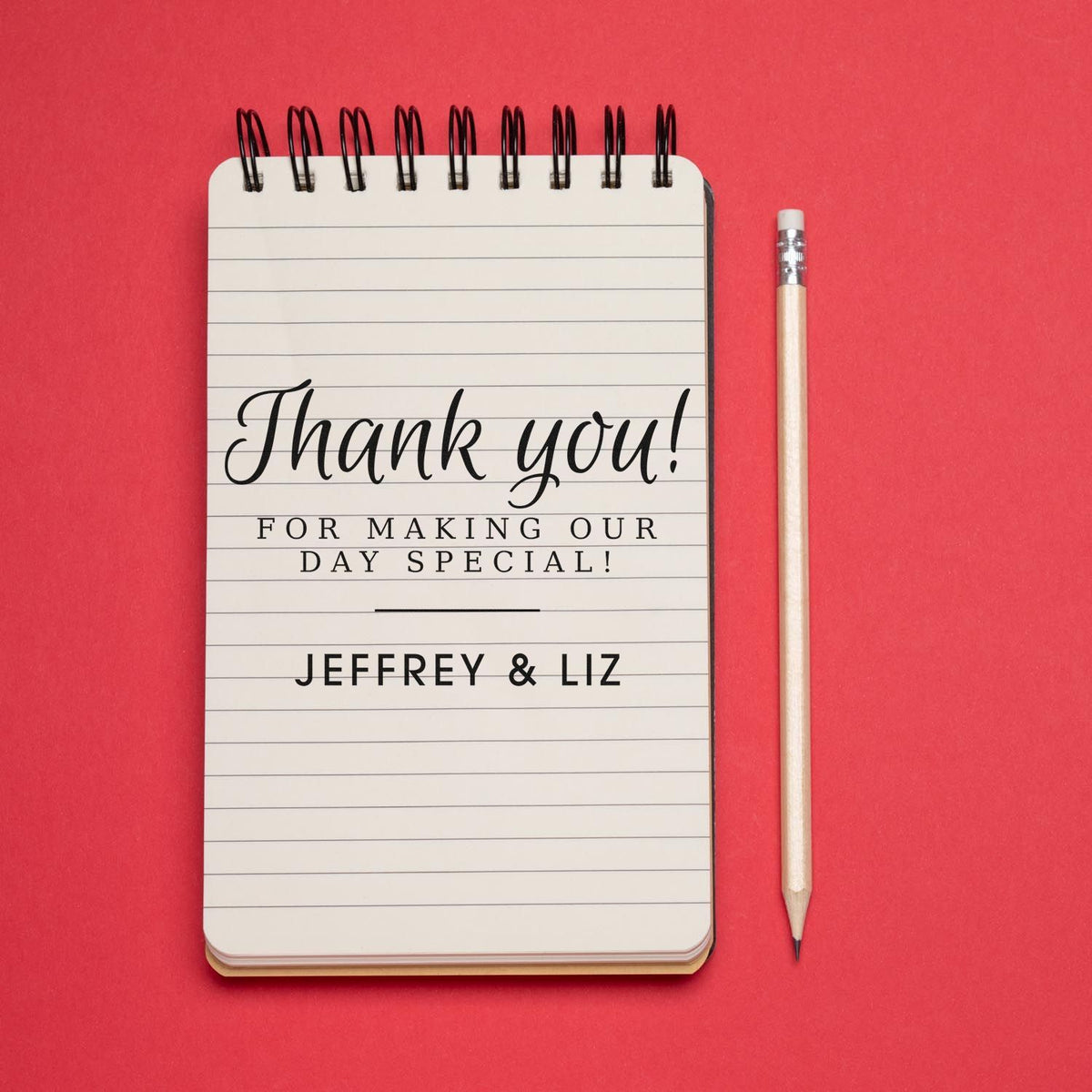Custom wedding thank-you stamp and seal notebook, white with black lettering, beside a pencil on a bright red background.
