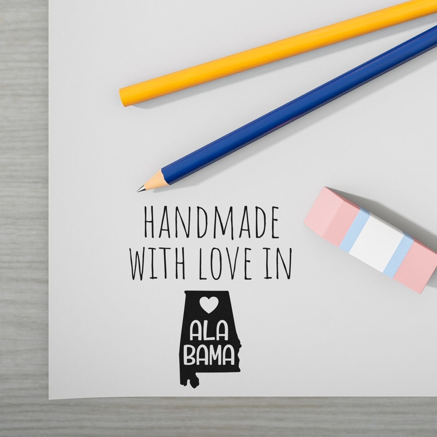 Self-Inking Alabama Handmade with Love Stamp on paper, featuring a heart and state outline. Includes pencils and eraser. Perfect for crafts and personalized projects.