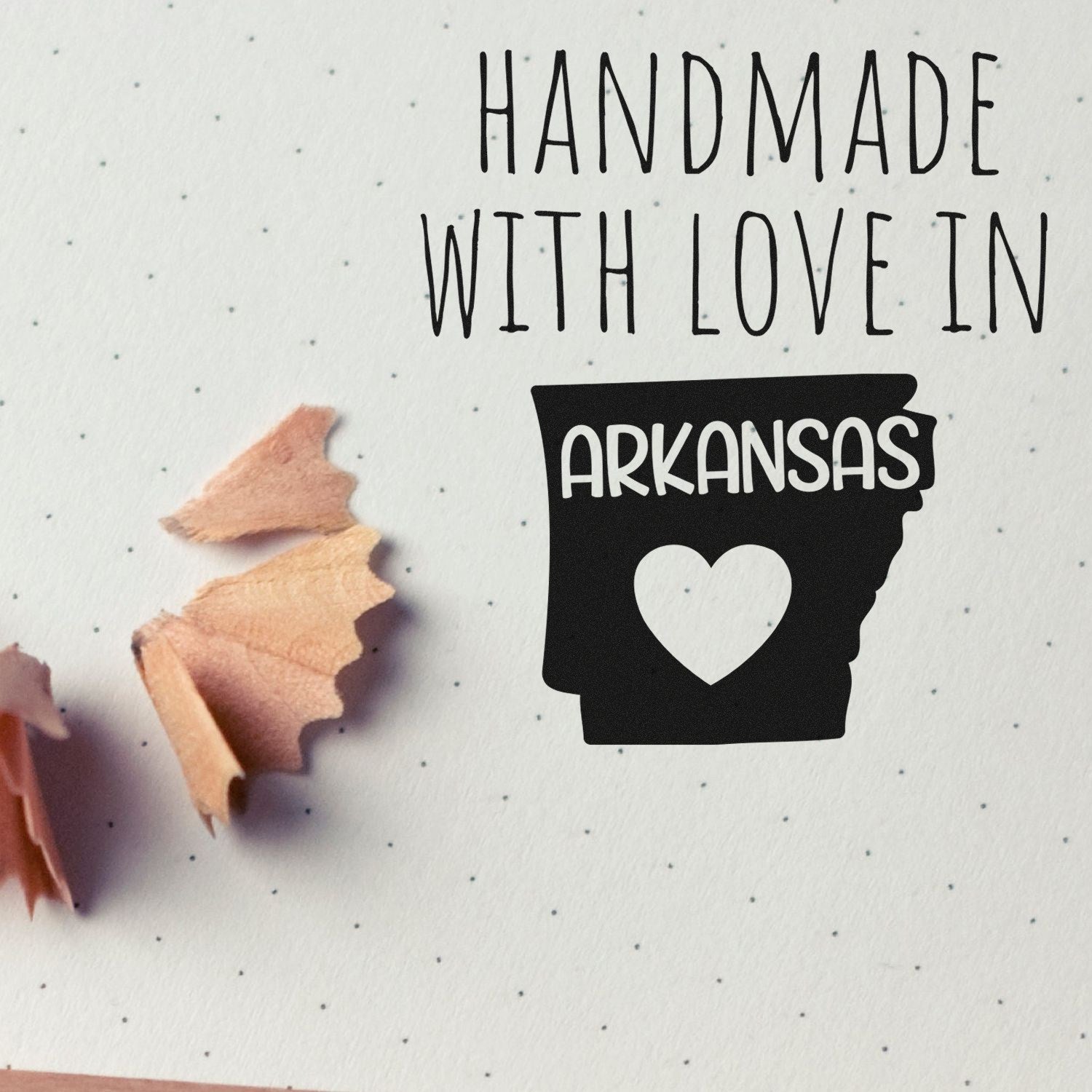 Self-Inking Arkansas Handmade with Love Stamp on dotted paper, featuring a heart and state outline, with pencil shavings nearby. Perfect for crafts and personalized projects.