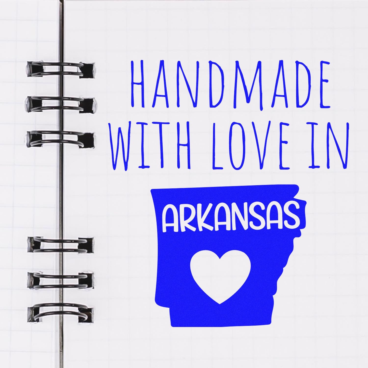 Handmade with Love in Arkansas Slim Pre-Inked Stamp featuring a blue Arkansas state outline with a heart, displayed on a notebook page.