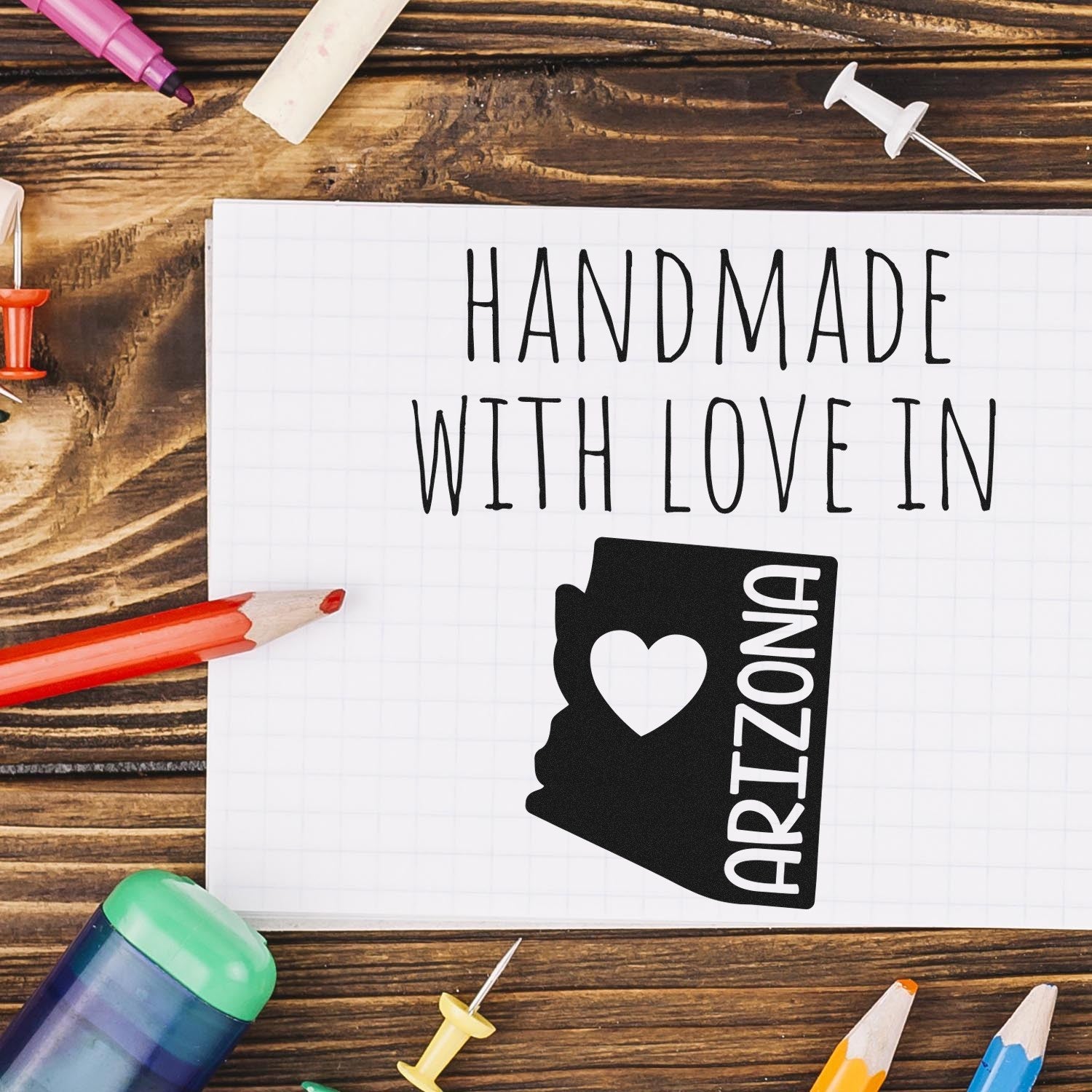 Self-Inking Arizona Handmade with Love Stamp on a notepad, surrounded by colorful stationery, showcasing its design with a heart and state outline. Perfect for crafts and personalized projects.