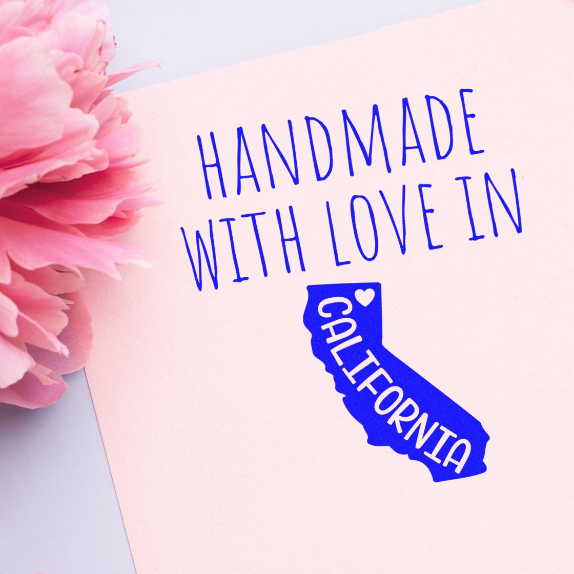 Wood Handle California Handmade with Love Rubber Stamp on pink paper with blue text and California outline, next to a pink flower.