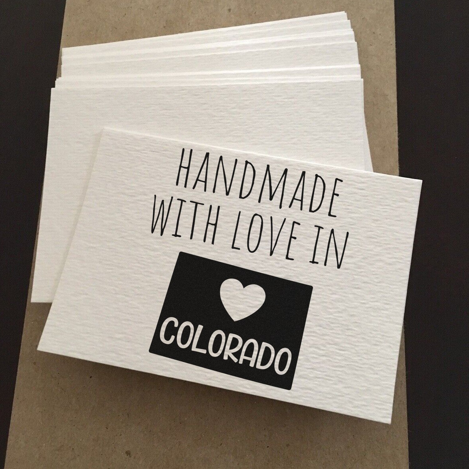 PSI Pre-Inked Handmade with Love in Colorado stamp on textured white cards, featuring bold black text and a heart design, showcasing artisanal craftsmanship.