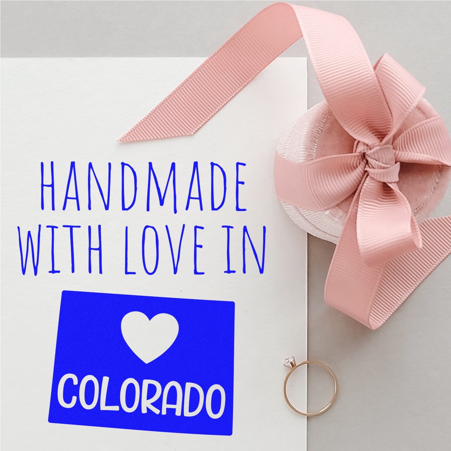 PSI Pre-Inked Handmade with Love in Colorado stamp on white card with pink ribbon and ring, showcasing a blue heart design and text.