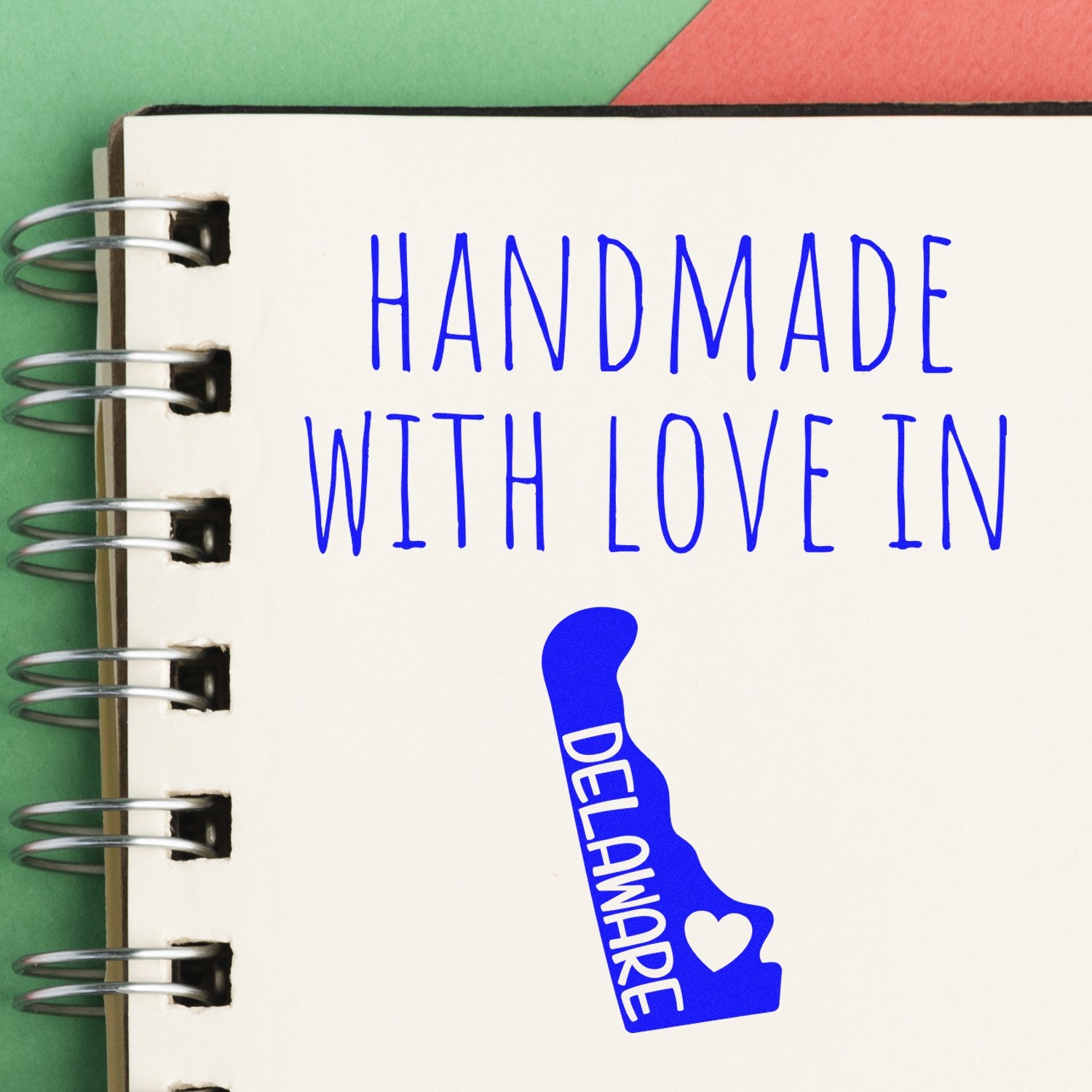 Self-Inking Delaware Handmade with Love Stamp on a notebook, featuring blue text and a Delaware state outline with a heart. Perfect for crafts and personalized projects.