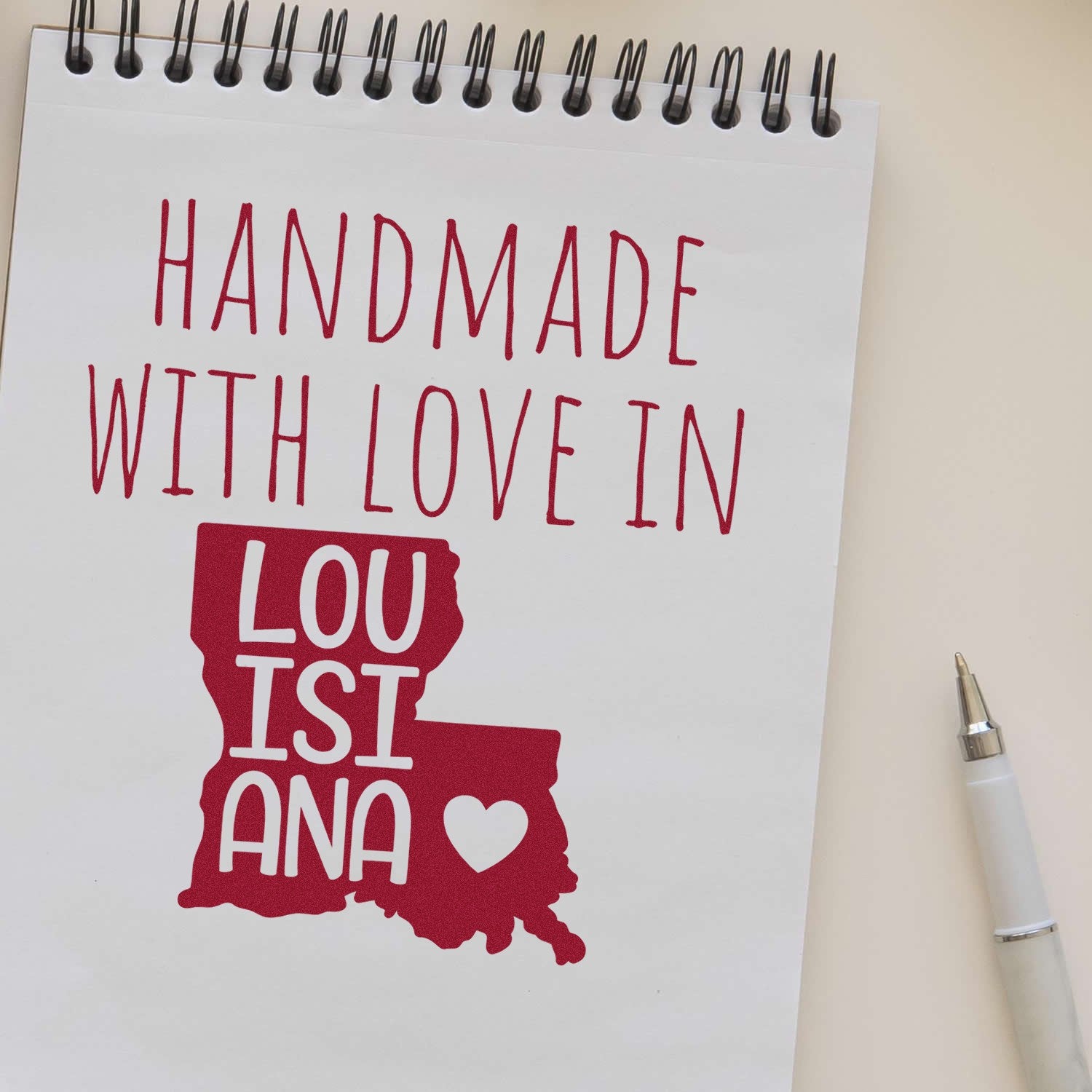 Handmade with Love in Louisiana Slim Pre-Inked Stamp on notepad, featuring red text and state outline with heart, alongside a pen. Perfect for personalized crafts and gifts.