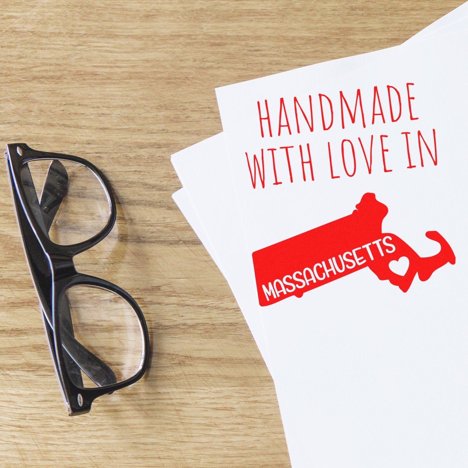 Handmade with Love in Massachusetts Slim Pre-Inked Stamp on paper, featuring a red state outline and heart, next to black glasses on a wooden surface.