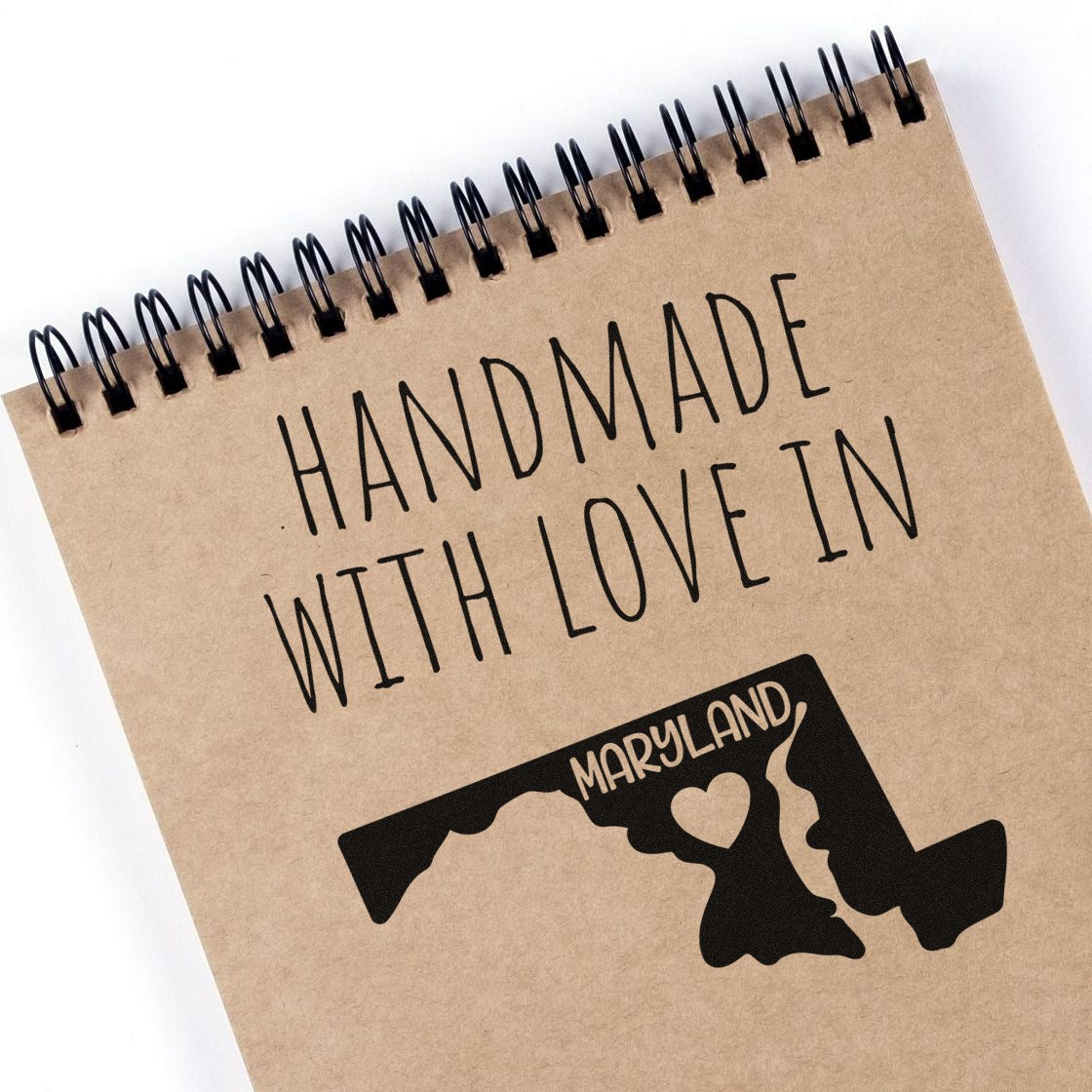 Handmade with Love in Maryland Slim Pre-Inked Stamp featuring a Maryland map design with a heart, displayed on a spiral notebook. Perfect for personalized crafts and gifts.