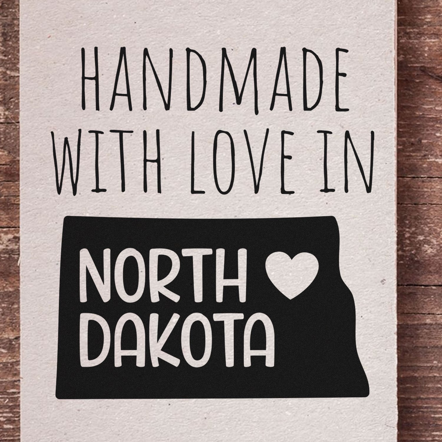 Handmade with Love in North Dakota Slim Pre-Inked Stamp on rustic wood background, featuring a heart and state outline design. Perfect for crafts and personalized projects.