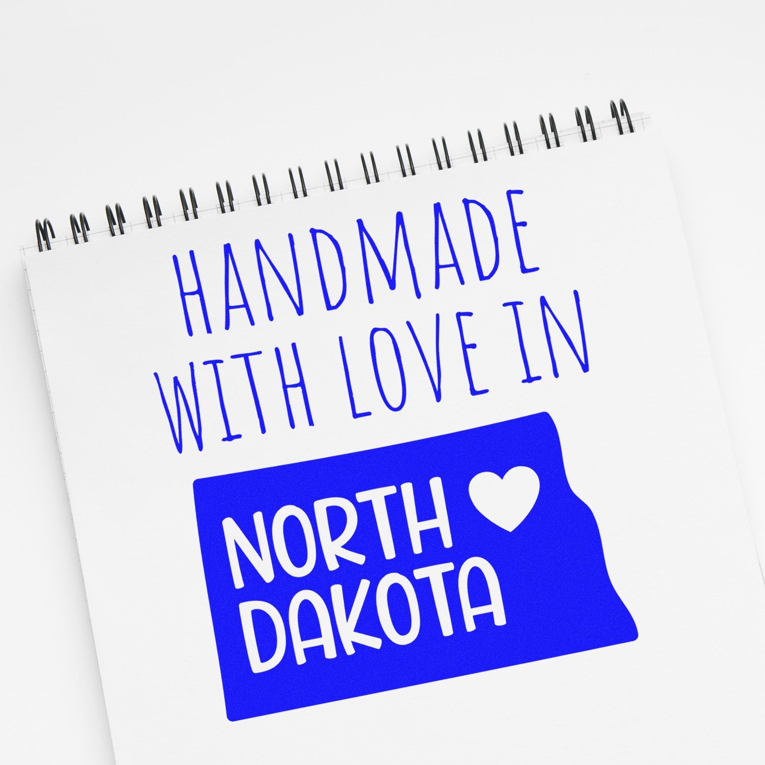 Self-Inking North Dakota Handmade with Love Stamp on a notepad, featuring blue text and a heart symbol, perfect for crafts and gifts.