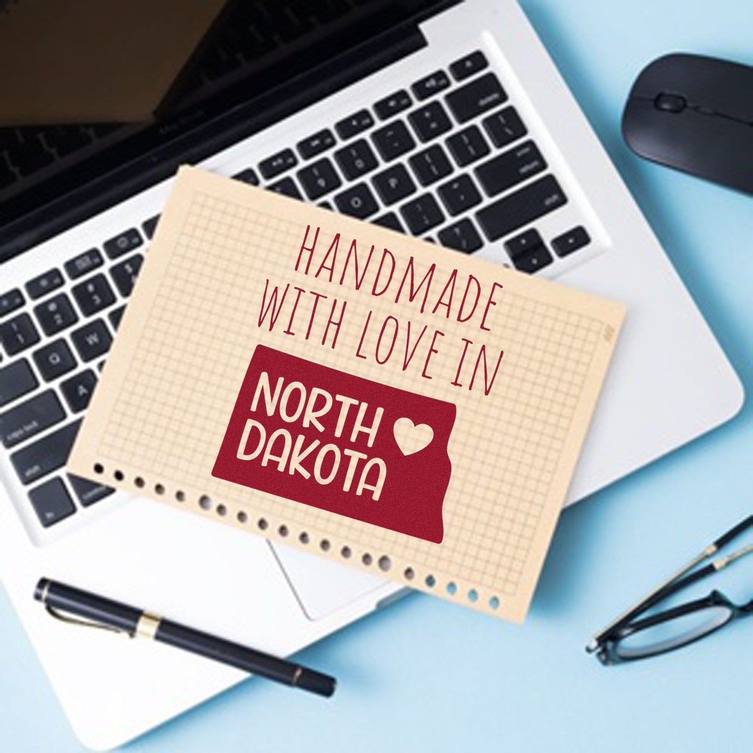 Wood Handle North Dakota Handmade with Love Rubber Stamp on a notepad, featuring a red state outline and heart, placed on a laptop keyboard. Perfect for crafts and personalized projects.