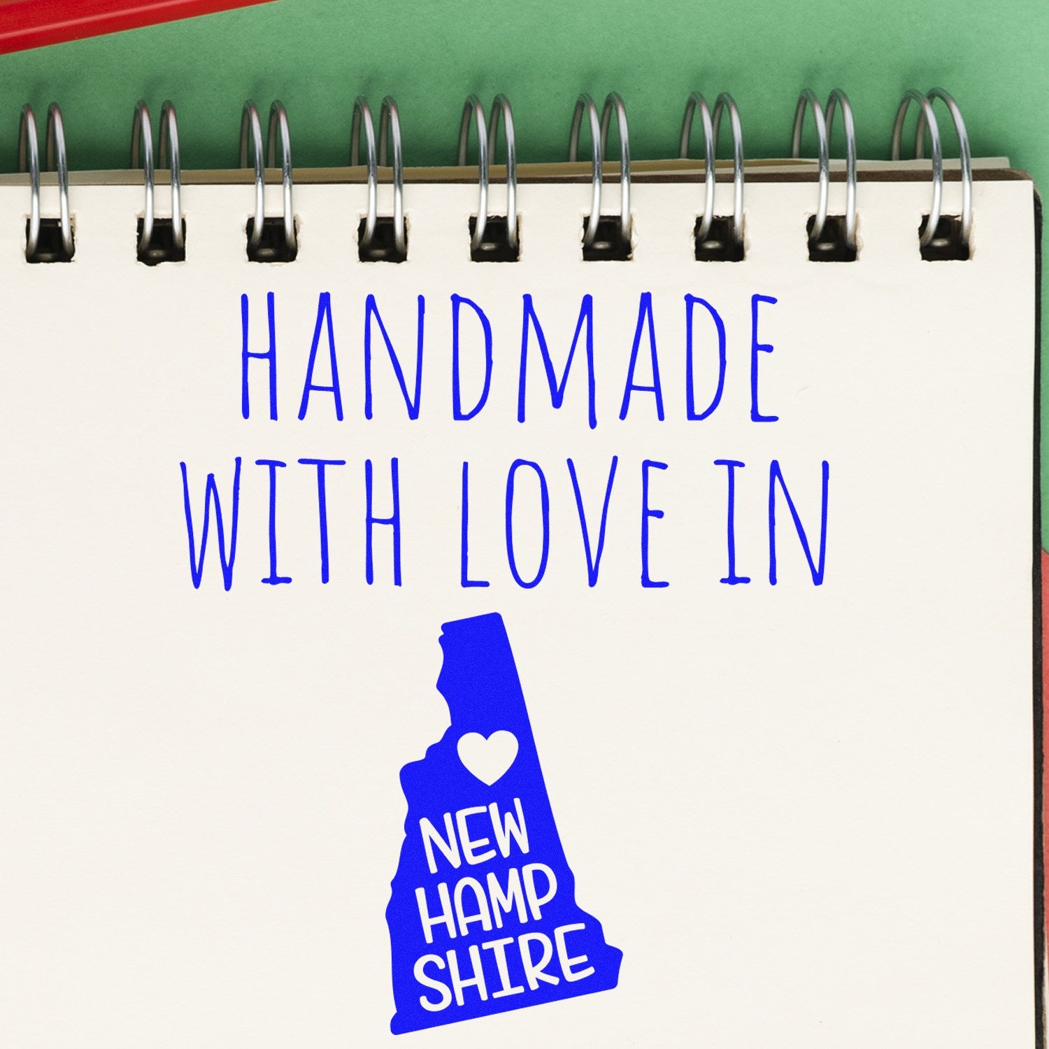 Wood Handle New Hampshire Handmade with Love Rubber Stamp on a notepad, featuring a blue New Hampshire state outline with a heart, emphasizing craftsmanship and local pride.