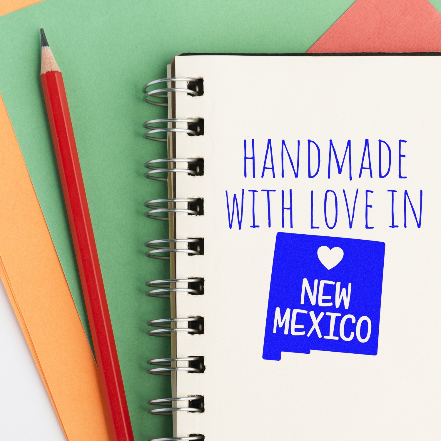 Wood Handle New Mexico Handmade with Love Rubber Stamp on a spiral notebook with colorful paper and a red pencil, showcasing the stamp's design and craftsmanship.