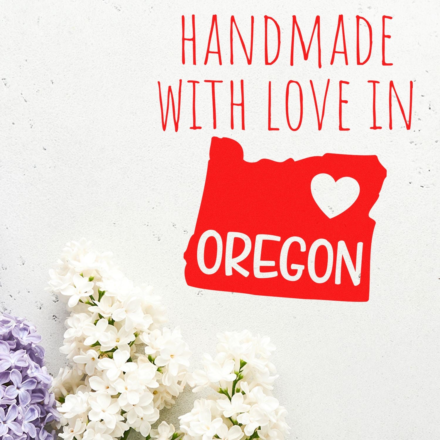 Self-Inking Oregon Handmade with Love Stamp featuring a red Oregon state outline with a heart, surrounded by white and purple flowers on a light background.