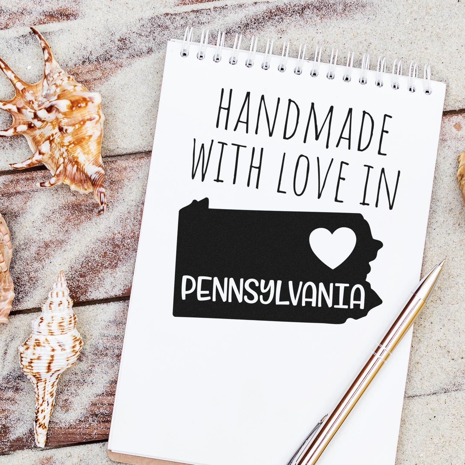 Handmade with Love in Pennsylvania Slim Pre-Inked Stamp on a notebook with seashells, showcasing a heart and state outline design. Perfect for adding a personal touch to crafts and letters.