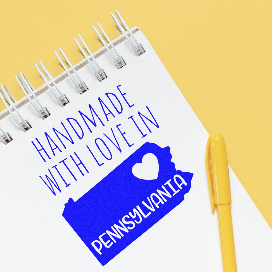 Self-Inking Pennsylvania Handmade with Love Stamp on notepad, featuring blue state outline and heart design, with yellow pen on a yellow background. Perfect for crafts and gifts.