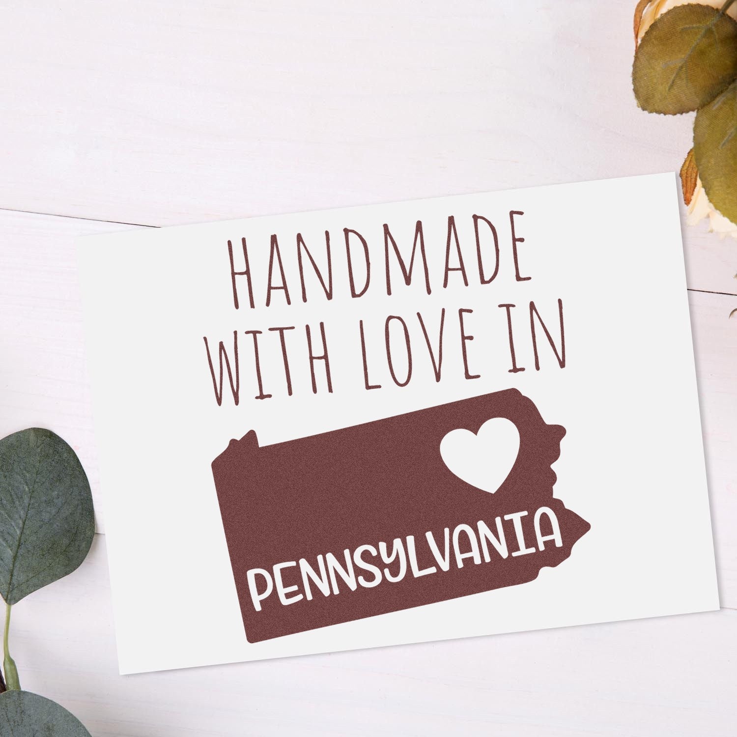 PSI Pre-Inked Handmade with Love in Pennsylvania stamp on white card with brown text and heart-shaped design, surrounded by green leaves on a light background.