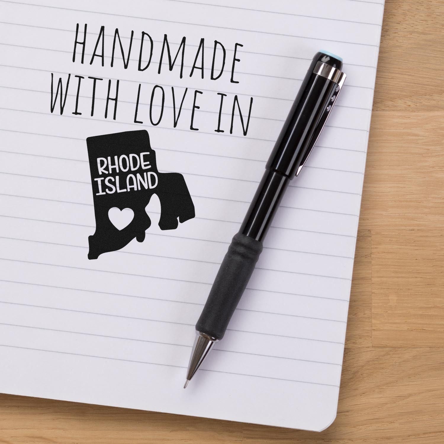 Wood Handle Rhode Island Handmade with Love Rubber Stamp on paper, featuring a map outline with heart design, next to a black pen. Perfect for crafts and personalized projects.