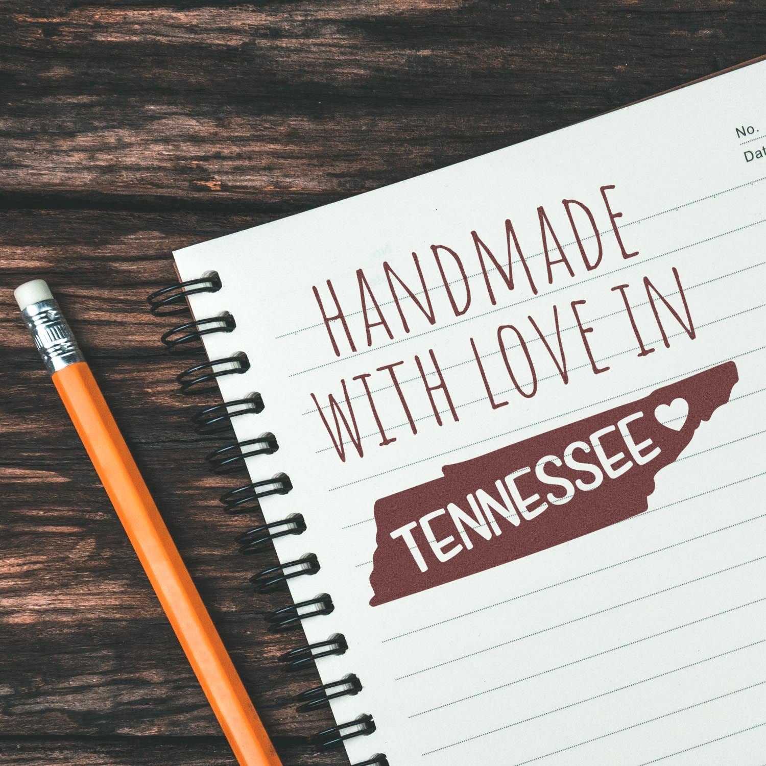 Image of a Wood Handle Tennessee Handmade with Love Rubber Stamp on a notebook, featuring the text Handmade with Love in Tennessee and a heart symbol, next to a pencil on a wooden surface.