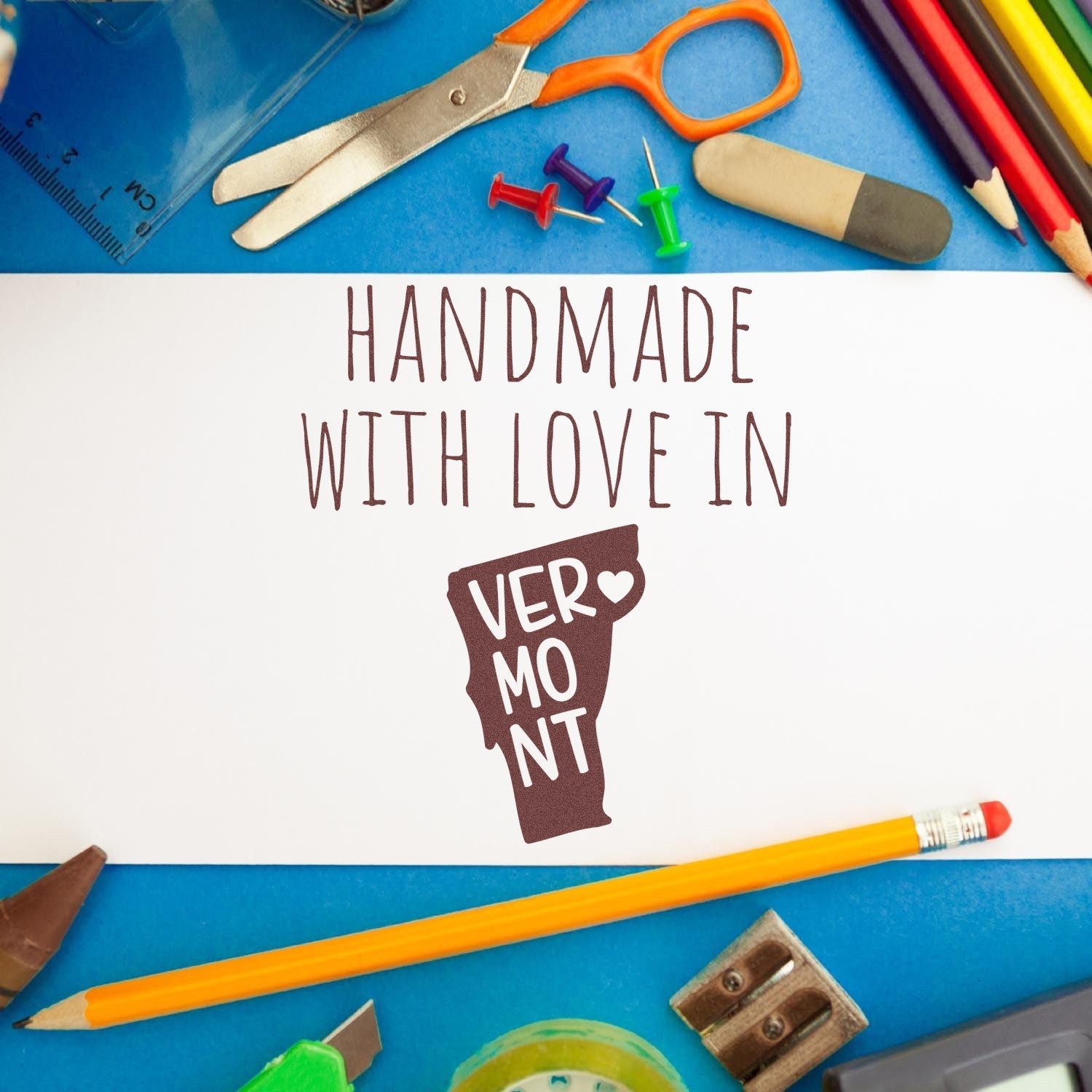 Handmade with Love in Virginia Slim Pre-Inked Stamp on a white card surrounded by colorful stationery, including scissors, pencils, and push pins. Perfect for crafting and personalized projects.