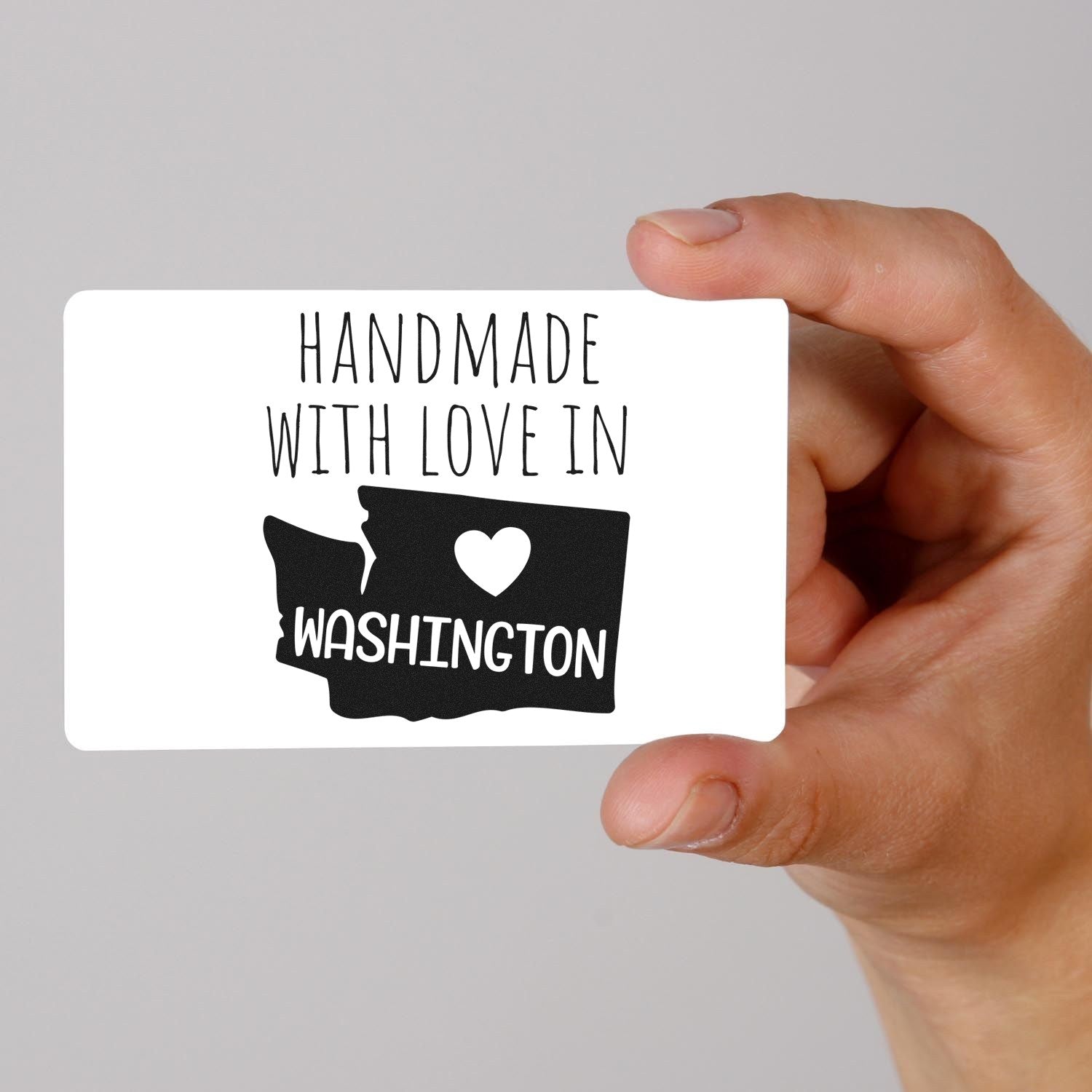 Hand holding PSI Pre-Inked 'Handmade with Love in Washington' stamp, featuring a heart and state outline design on a white background.