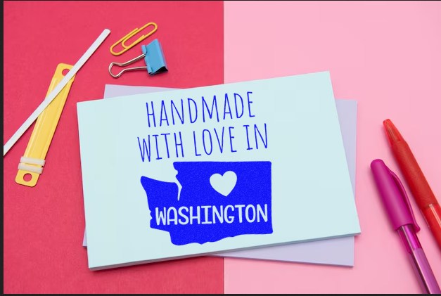 Wood Handle Washington Handmade with Love Rubber Stamp on a card with blue text and a heart, surrounded by office supplies on a pink and red background.