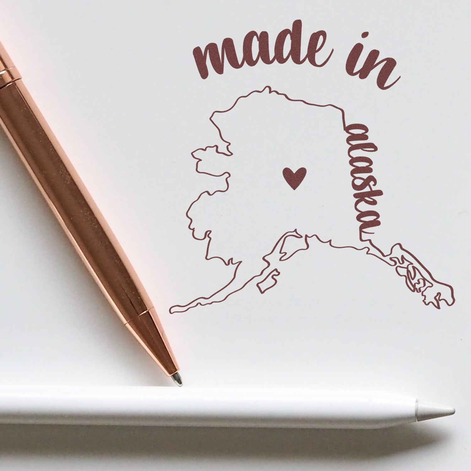 Made with Love in Alaska Rubber Stamp featuring a heart on the Alaska map, with 'made in alaska' text in brown. Includes a rose gold pen and white stylus for scale.