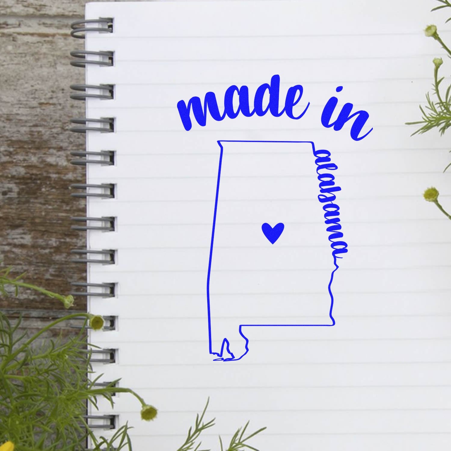 Self-Inking Handmade with Love in Alabama Stamp on a notebook, featuring a blue outline of Alabama with a heart, and made in Alabama text. Perfect for crafts and personalized projects.