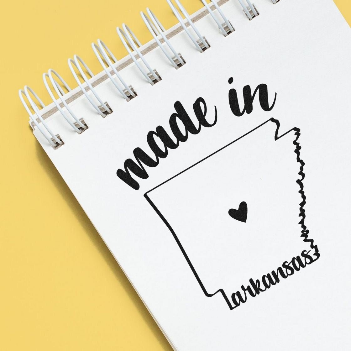 Made in Arkansas Stamp Pre-Inked on a notepad, featuring a heart inside the state outline, with 'made in' text above. Perfect for adding a personal touch to crafts and stationery.