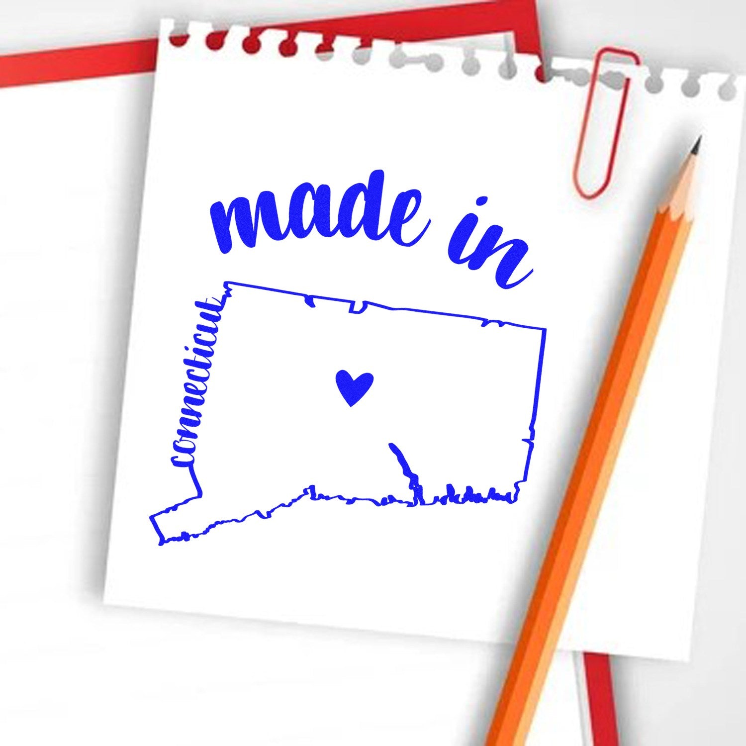 Made with Love in Connecticut Rubber Stamp featuring a blue outline of Connecticut with a heart, displayed on a notepad with an orange pencil and red paperclip.