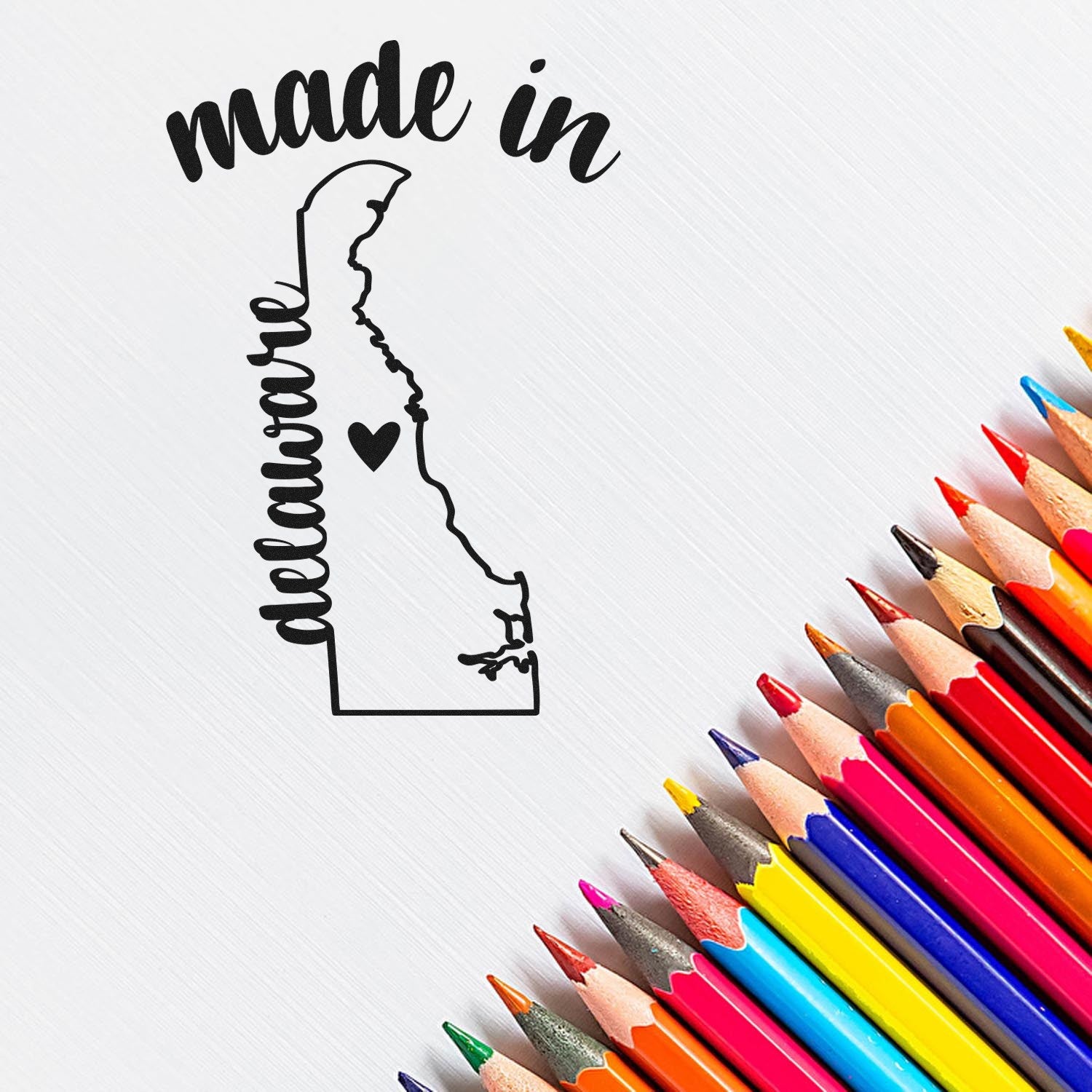 Made with Love in Delaware Rubber Stamp featuring a heart and state outline, displayed on a white background with colorful pencils. Perfect for crafts and personalized projects.