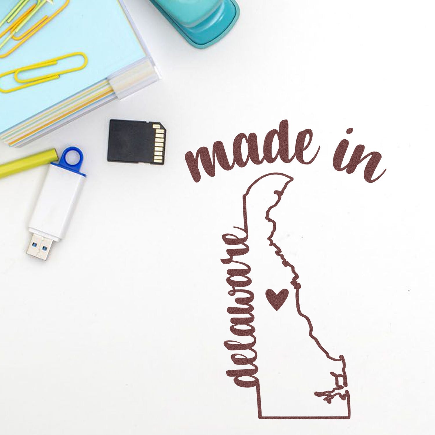 Made with Love in Delaware Rubber Stamp featuring a heart and state outline, surrounded by office supplies on a white background.